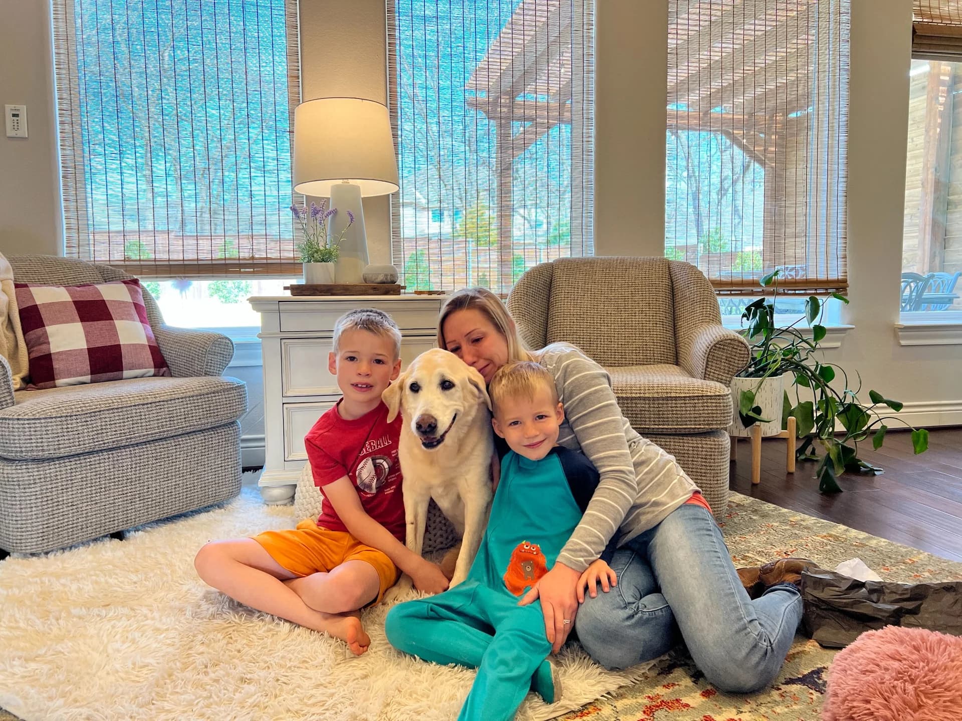 Aubree Felderhoff smiling on the living room rug with her two boys and their dog