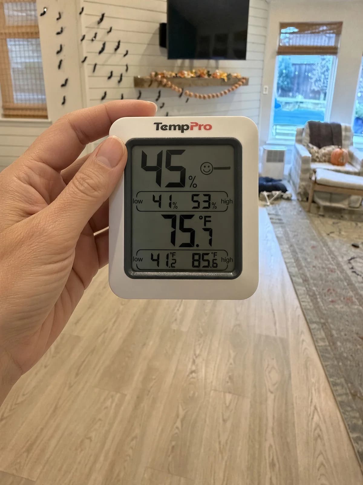 Hand holding a TempPro humidity meter reading 45 percent humidity and 75.7 degrees in a living room